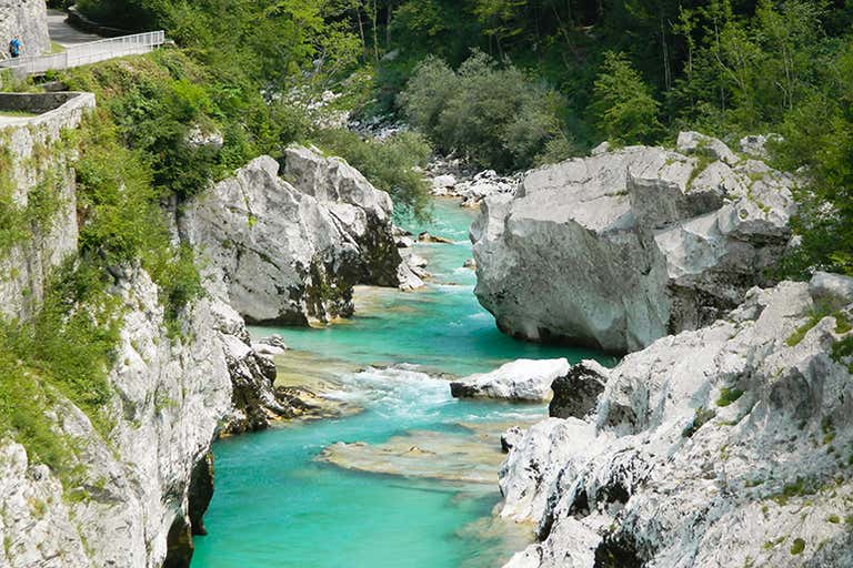 A serene river surrounded by lush green trees and hills under a blue sky.