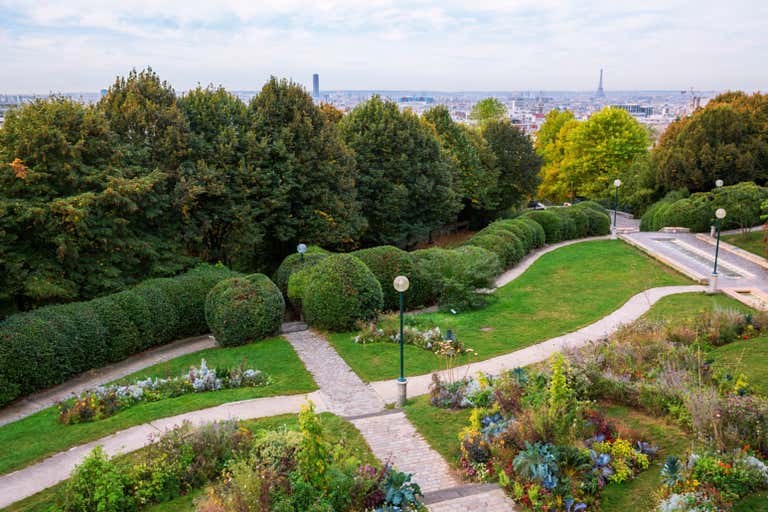 A scenic view of Paris from a lush green park with pathways, trees, and the Eiffel Tower visible in the distance.