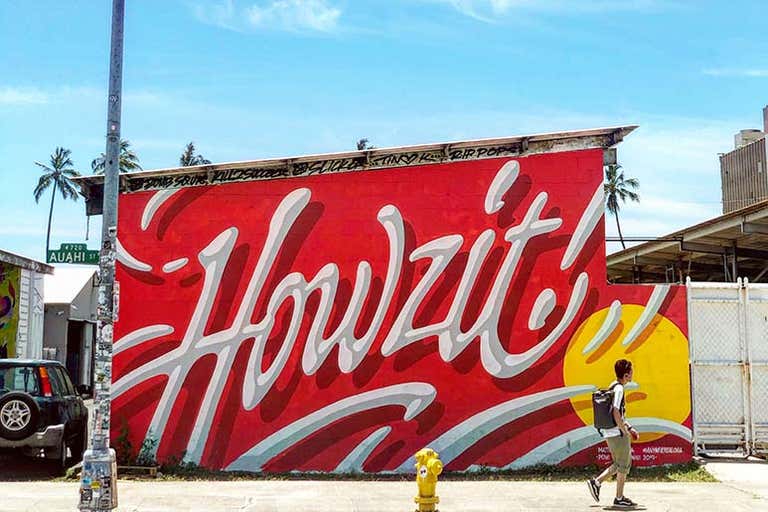 Bold "Howzit" mural in Honolulu’s Kakaʻako neighborhood with palm trees in the background.