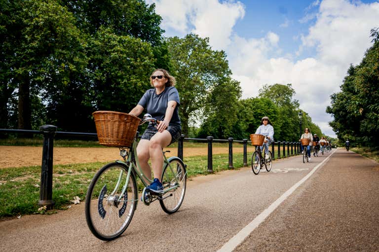 Cyclists riding on a path in Hyde Park, London, surrounded by trees.