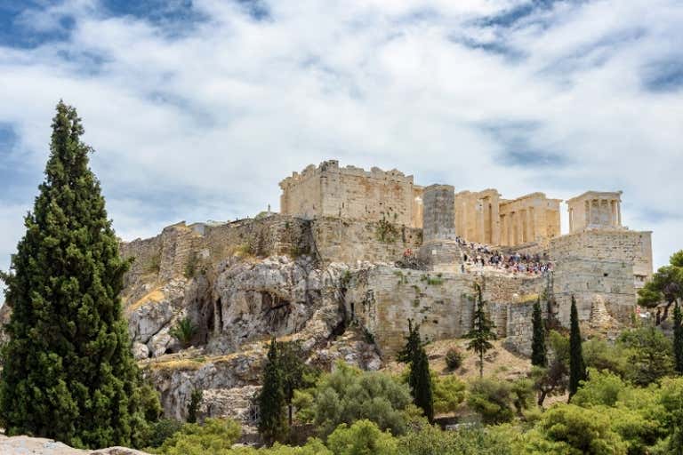 View of the Acropolis in Athens with a cloudy sky and greenery.