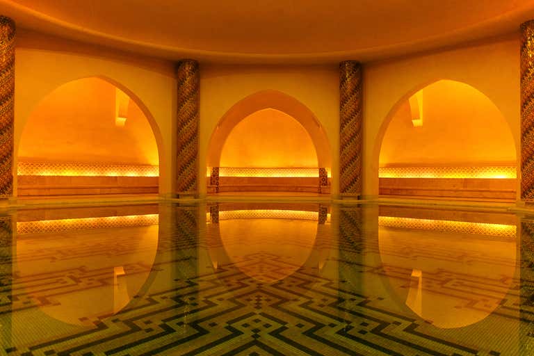 El interior de un hammam marroquí, con arcos cálidamente iluminados que se reflejan en el agua.