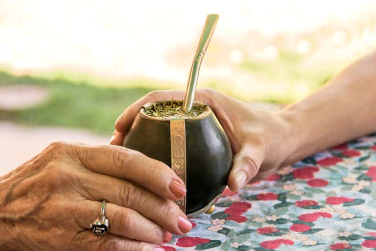 Duas mãos segurando um copo de mate tradicional com um canudo de metal.