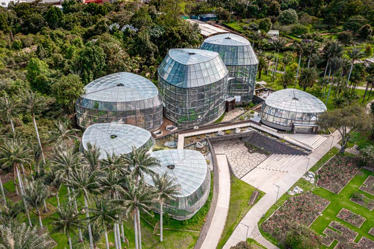 Aerial view of Bogotá’s Botanical Garden featuring glass-domed greenhouses surrounded by lush greenery and palm trees.