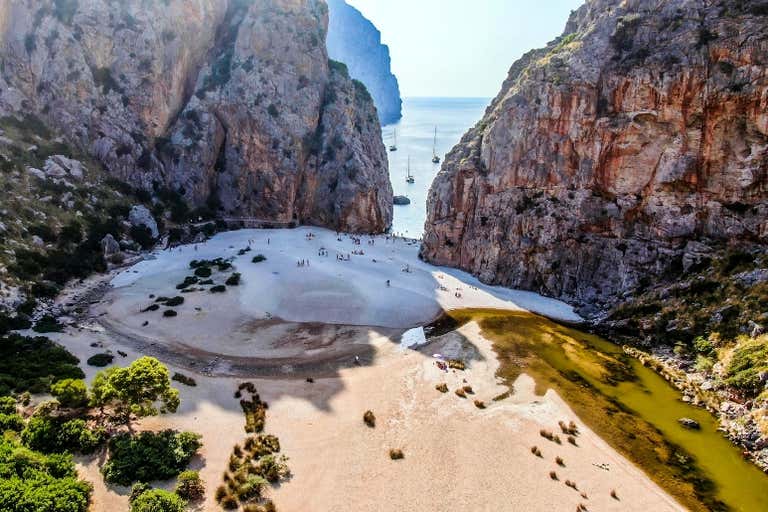 Aerial view of a sandy beach surrounded by high cliffs with boats in the distance.
