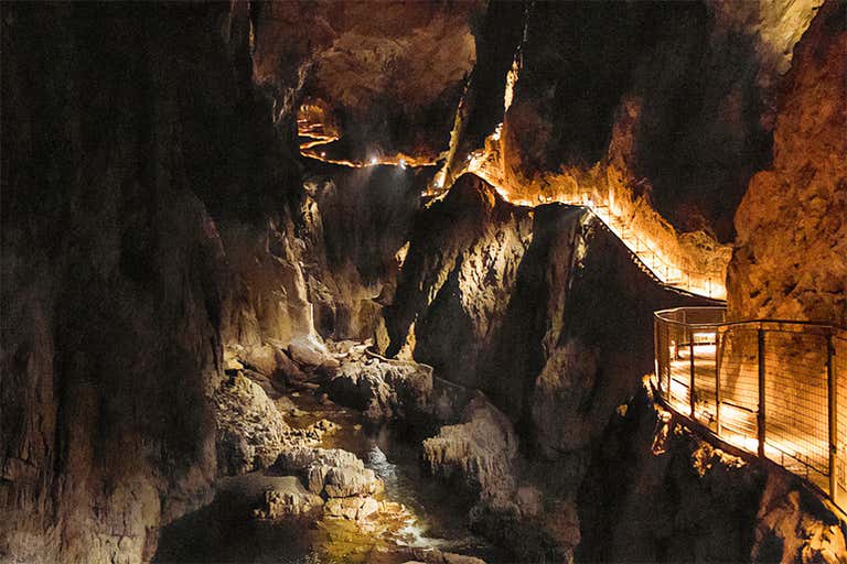 Illuminated walkway through dramatic underground cavern of Škocjan Caves, with dramatic limestone formations and deep gorge below