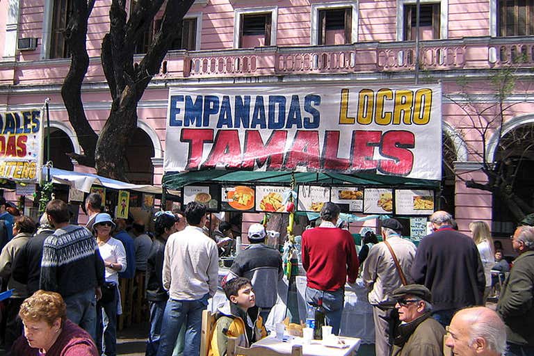 Street food vendor selling empanadas and tamales with crowd of people in Buenos Aires.