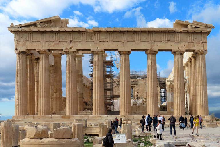 Het Parthenon in Athene met toeristen eromheen, onder een blauwe hemel