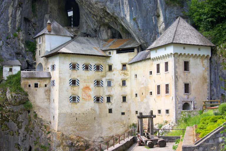 Medieval Predjama Castle built into a cave mouth, featuring white fortress walls with striped window shutters and Renaissance architecture