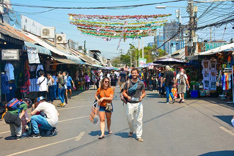 Люди гуляют по оживлённому рынку на свежем воздухе под яркими украшениями над головой.