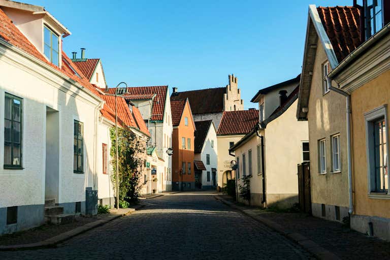Rua estreita de paralelepípedos em Visby com edifícios medievais coloridos e telhados de telhas vermelhas.