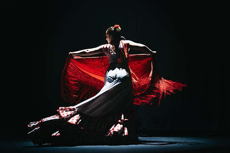 A flamenco dancer performing on stage with a red shawl.
