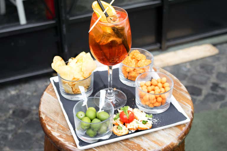 Ein Tablett mit einem Aperol Spritz und verschiedenen Häppchen auf einem Holztisch.