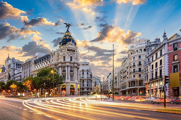 Uma paisagem urbana vibrante da Gran Vía em Madri durante o pôr do sol com rastros de luz dos carros.