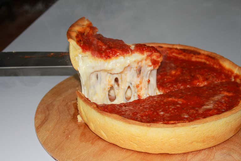 Una porción de pizza estilo Chicago se levanta de una pizza entera sobre una tabla de madera.