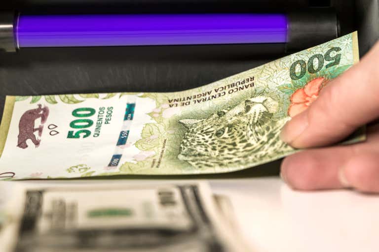 Uma pessoa verificando a autenticidade de uma nota de 500 pesos argentinos sob uma luz UV.
