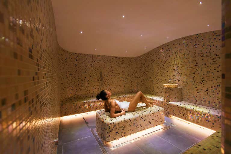 Una mujer se relaja en un hammam spa con azulejos de mosaico.