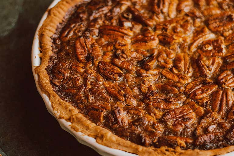Golden-brown pecan pie with a flaky crust, topped with caramelized pecans, served in a white ceramic dish.
