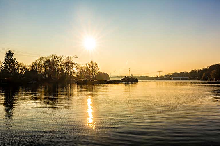 A sunrise over a calm river with trees and power lines in the background.