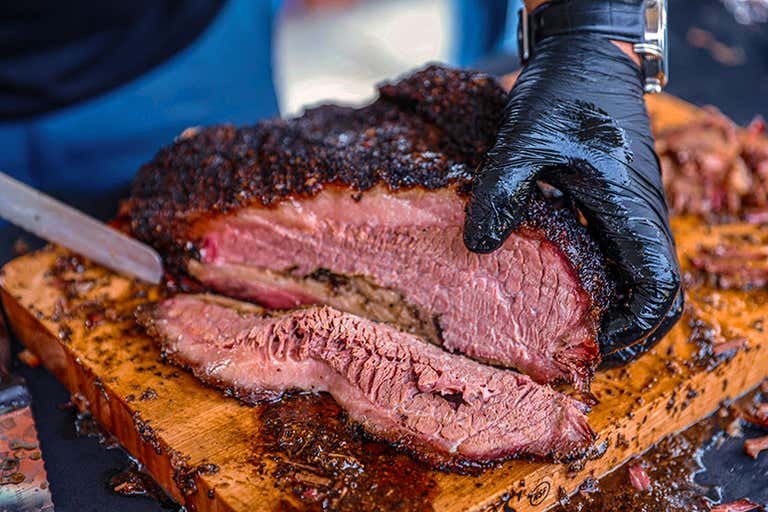 Smoked brisket with a charred crust being sliced on a wooden board, revealing juicy pink meat inside.