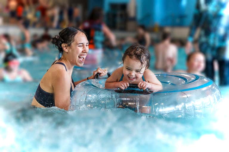 Uma mulher e uma criança curtindo uma piscina com outras pessoas ao fundo.