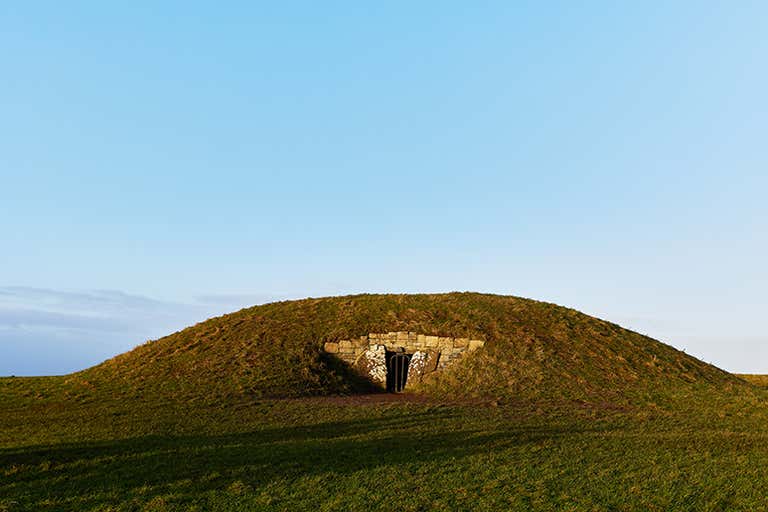 A grassy mound with a stone entrance under a clear blue sky.