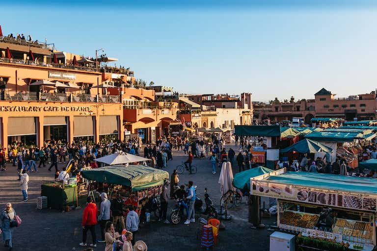 Una bulliciosa plaza de Marrakech con gente y puestos de mercado al amanecer.