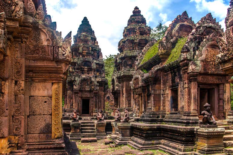 Ancient Khmer temple ruins at Banteay Srei, Cambodia with intricate stone carvings, moss-covered towers, and guardian statues.