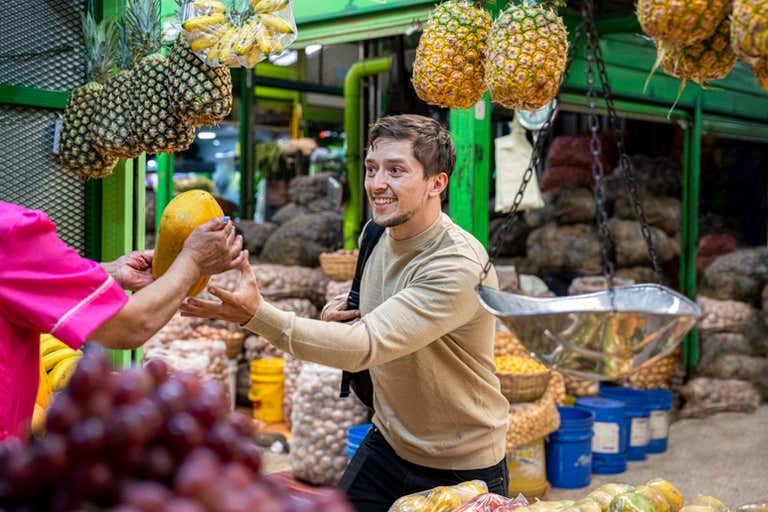 A vendor handing a papaya to a customer at Bogotá’s Paloquemao Market, surrounded by tropical fruits and produce.