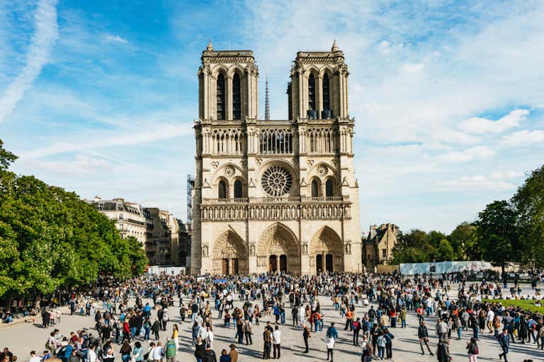 Notre Dame Cathedral's Gothic facade with twin towers, rose window and three arched entrances with crowds gathered in front