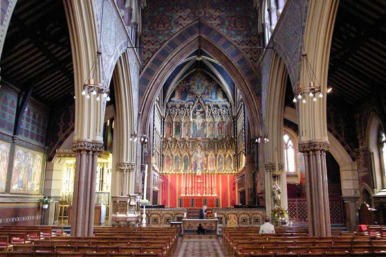 Interior of All Saints Church with richly decorated altar, painted arches, colorful walls and wooden pews in dim lighting