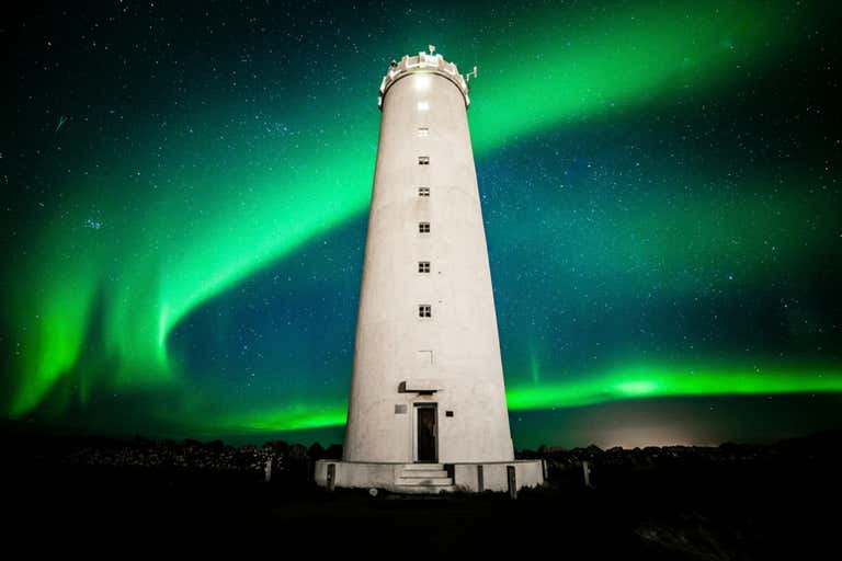 Un faro bajo la aurora boreal en Islandia por la noche.