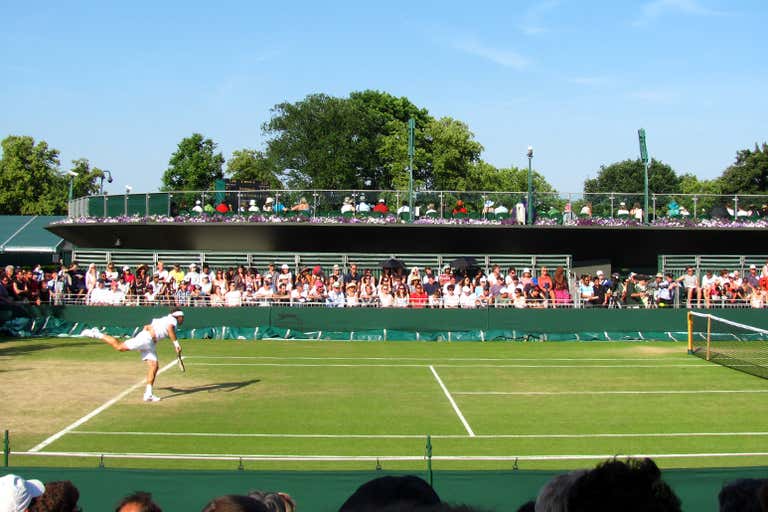A tennis match in progress on a grass court with spectators watching.