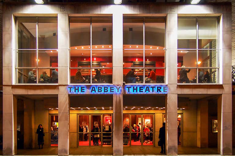 El exterior del Teatro Abbey de Dublín (Irlanda), iluminado por la noche con personas visibles en su interior.