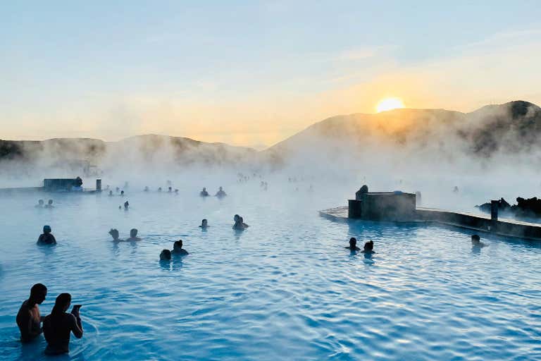Gente disfrutando de la Laguna Azul en Islandia al atardecer con el vapor saliendo del agua.