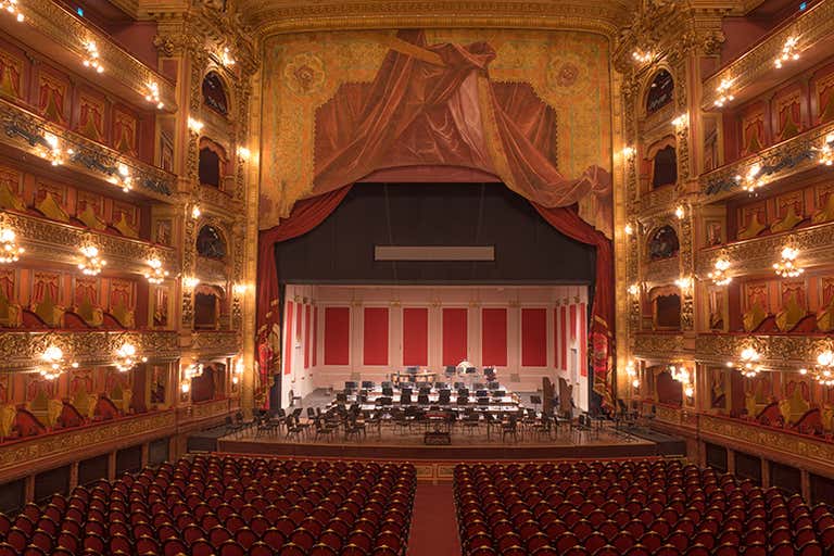 Vista interna do Teatro Colón com decorações ornamentadas e assentos vazios.
