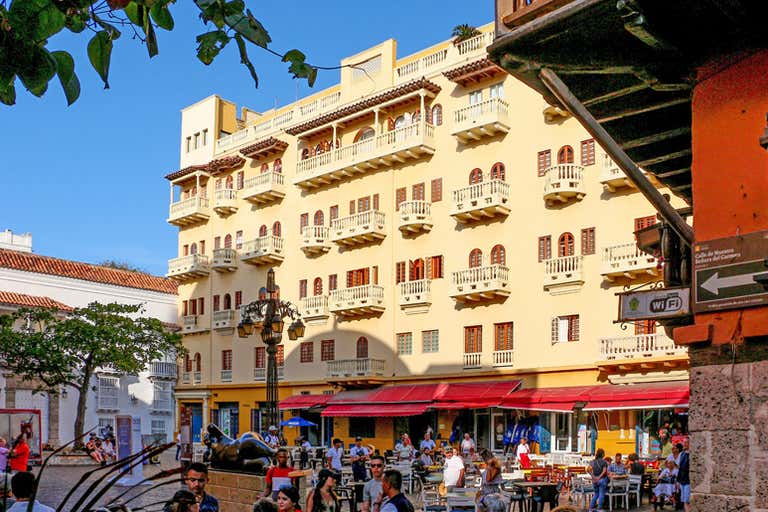 A bustling plaza in Cartagena with a historic yellow building and outdoor cafes.