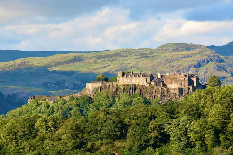 Eine historische Burg, die auf einem Hügel thront, umgeben von üppigem Grün und Hügeln.