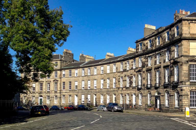 A curved row of Georgian townhouses on a sunny day in Edinburgh.