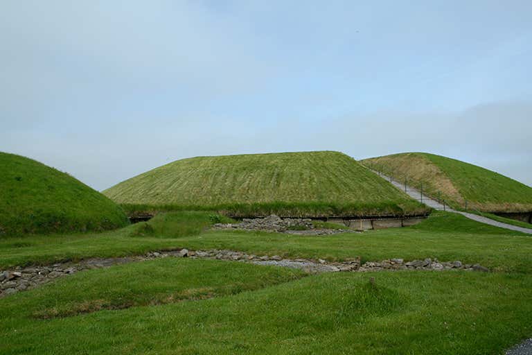 A grassy mound with stone structures at Knowth, part of the Brú na Bóinne complex in Ireland.