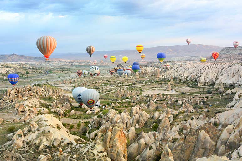 Coloridos globos aerostáticos flotando sobre las singulares formaciones rocosas y el paisaje de los valles de Capadocia, Türkiye, durante un vuelo matutino.