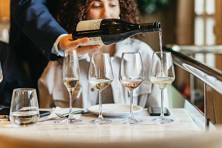 Een persoon schenkt wijn in glazen aan een restauranttafel