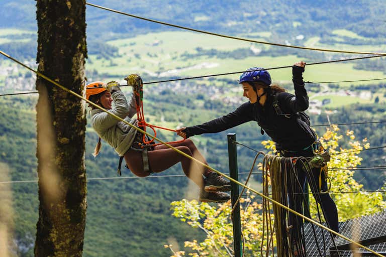 Instructor assists zipline rider on Europe's longest zipline course in Planica, Slovenia, with green valley views stretching below