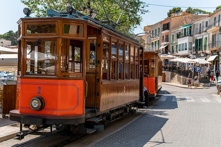 A vintage wooden tram in Sóller, Mallorca, with colorful buildings and outdoor cafes in the background.