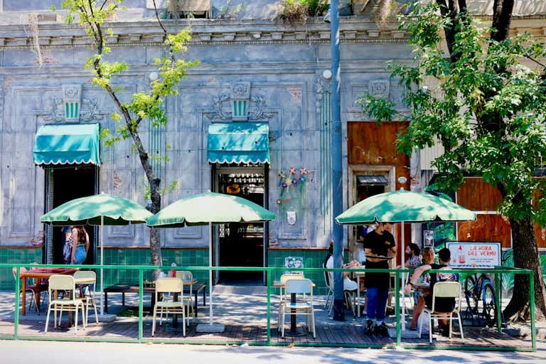 Área de estar ao ar livre de um café com guarda-chuvas verdes e uma fachada vintage.