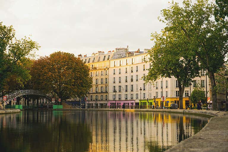 Canal view in Paris with colorful buildings and trees reflected in the water under a soft evening light.