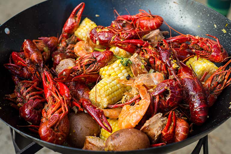 A Cajun seafood boil with crawfish, shrimp, corn, potatoes, and sausage served in a large black skillet.