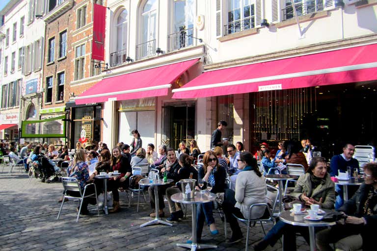 People sitting at outdoor cafe tables under red awnings in Brussels.