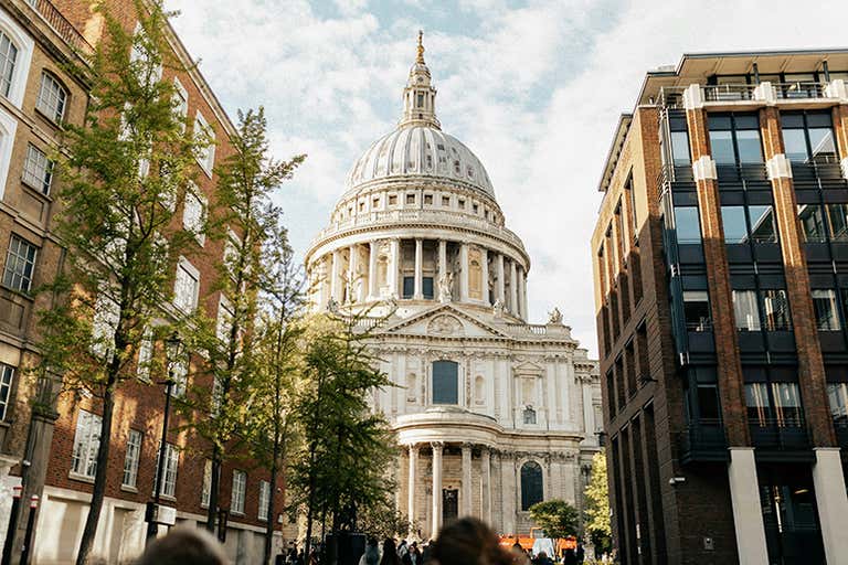 St. Paul's Cathedral's iconic white dome and classical facade framed by modern buildings and trees in the City of London
