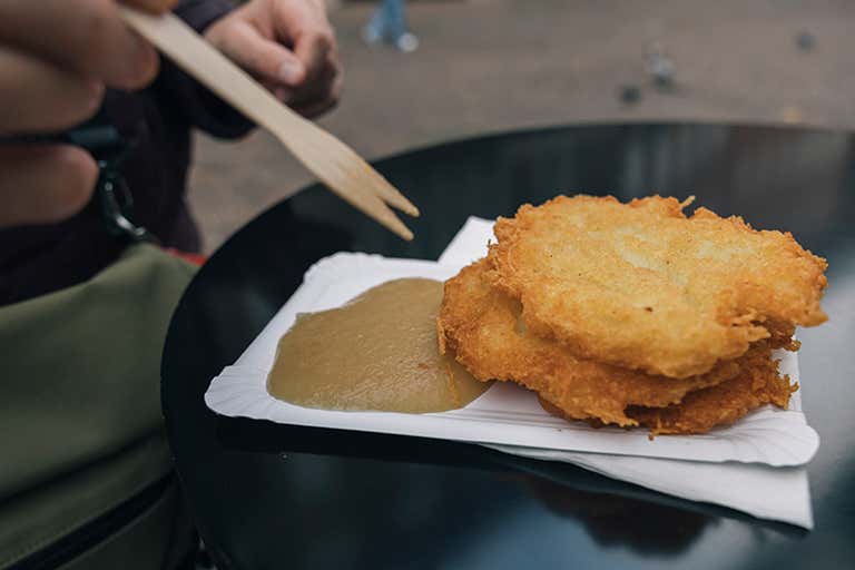 A person with a wood fork by a plate of potato pancakes with applesauce